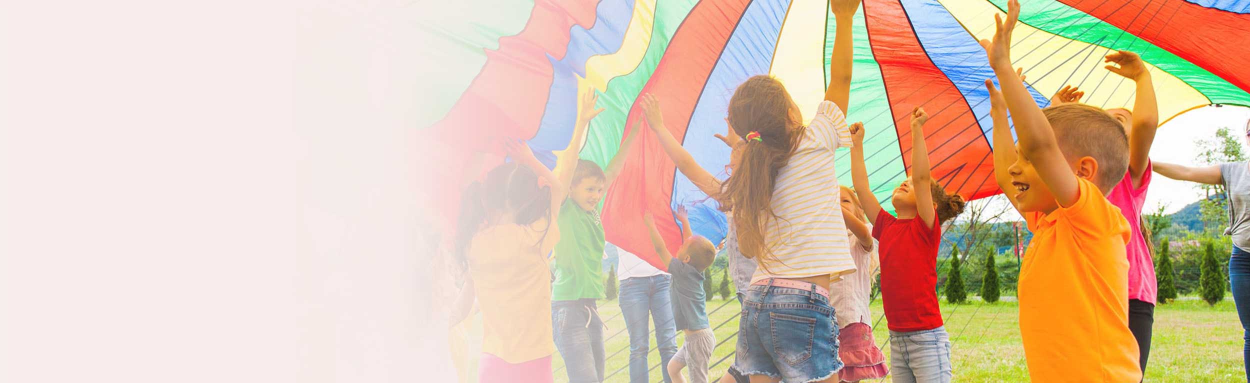 Joyous classmates jumping under colorful parachute in the summer
